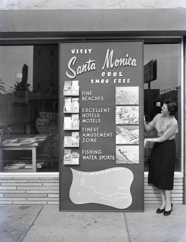 Visit Santa Monica, 1955 Woman standing next to a sign that reads "Visit Santa Monica"