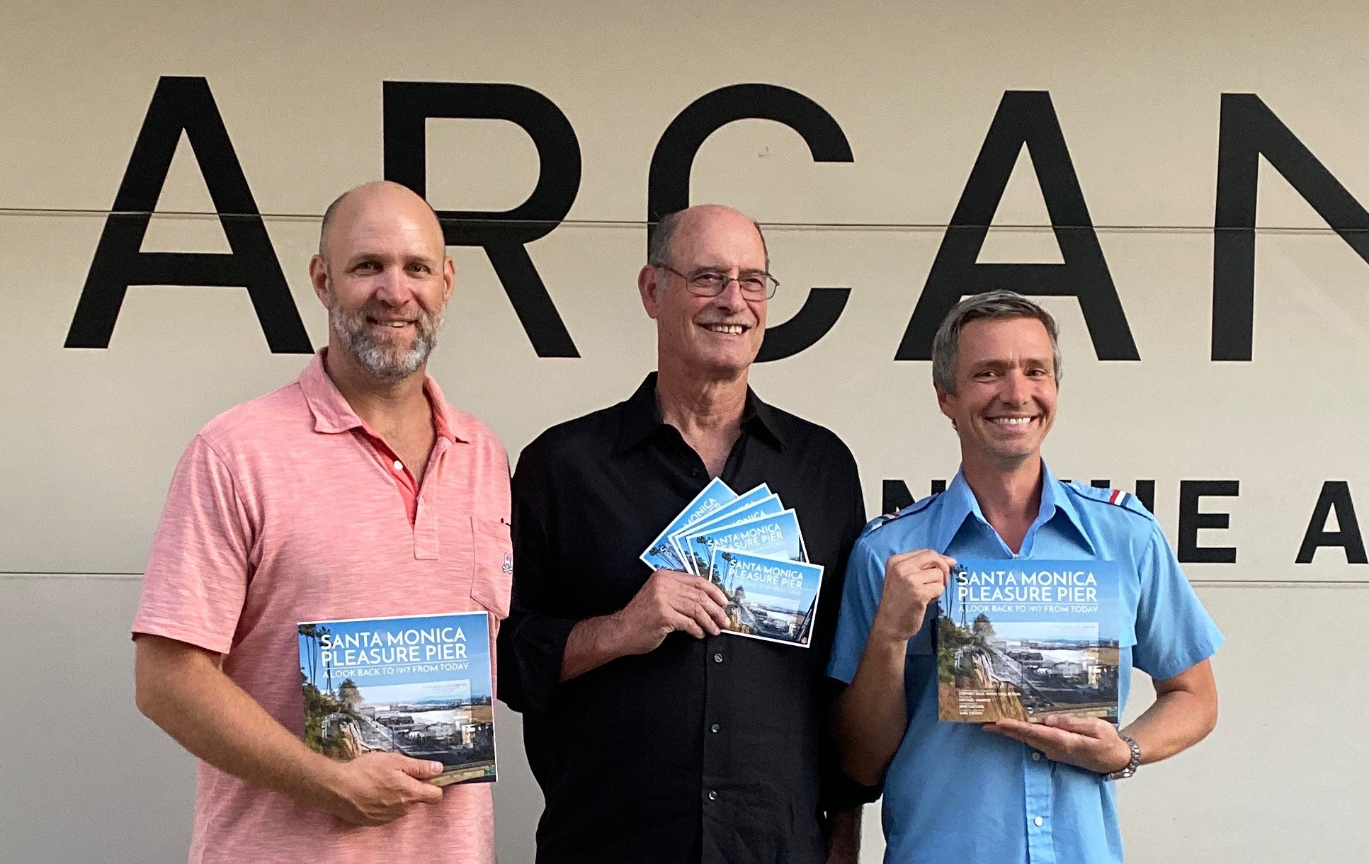 Group photo of Michael Murphy, Stephen Anaya, Jens Lucking holding their book "Santa Monica Pleasure Pier"