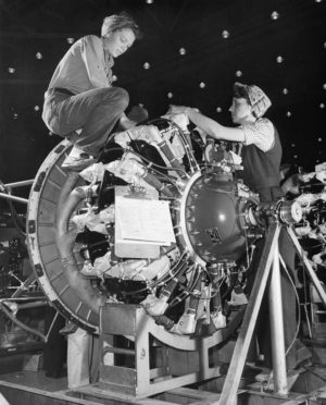 Two women employees, in the genre of "Rosie the Riveter," working on an aircraft engine at the Douglas Aircraft Company