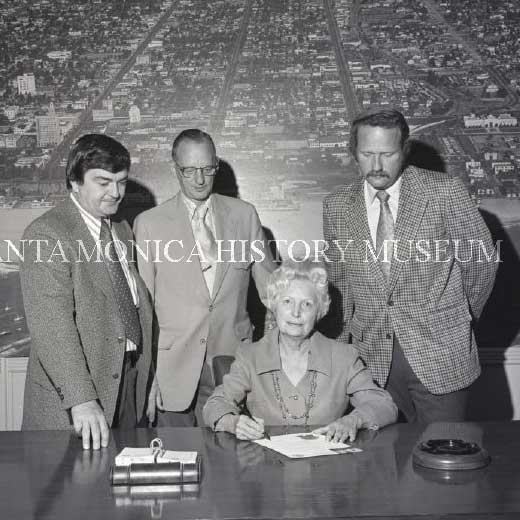 Mayor Clo Hoover sitting at a table with doucments and 3 men standing behind her
