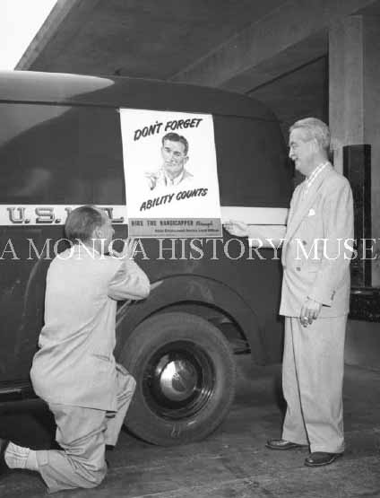 Two men standing by mail truck with poster for national employ the physically handicap week