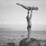Gymnasts Glenn Sundby lifted by George Long while standing on rocks at the beach