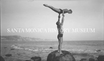 Gymnasts Glenn Sundby lifted by George Long while standing on rocks at the beach