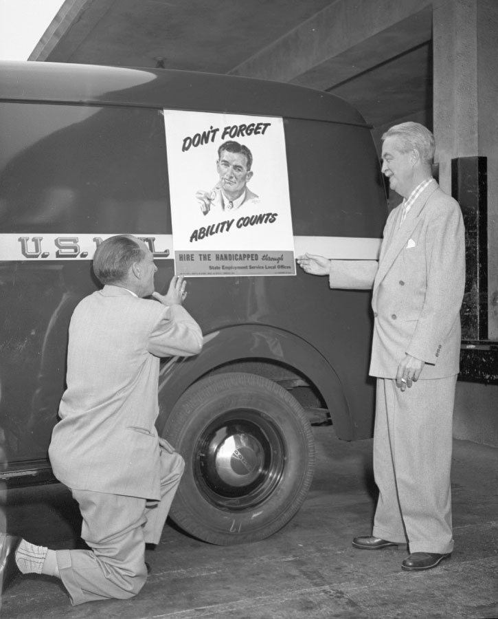 Two men standing by mail truck with poster for national employ the physically handicap week