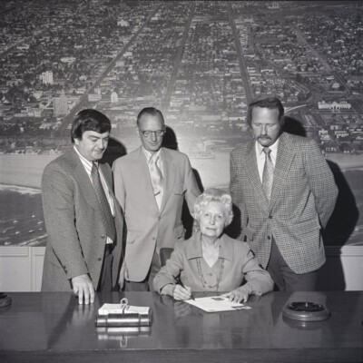Mayor Clo Hoover sitting at a table with doucments and 3 men standing behind her