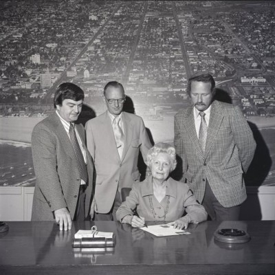 Mayor Clo Hoover sitting at a table with documents and 3 men standing behind her